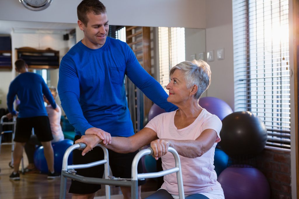 Physiotherapist assisting senior woman patient to walk with walking frame